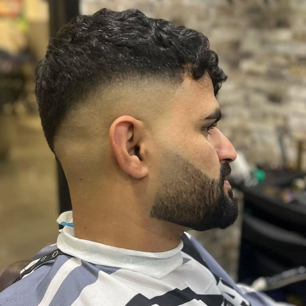 Curly top with a skin fade and full beard, in profile