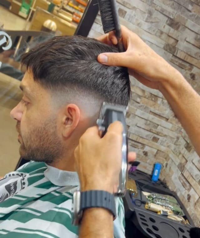 Clippers in hand, mid-cut against the shop's brick feature wall